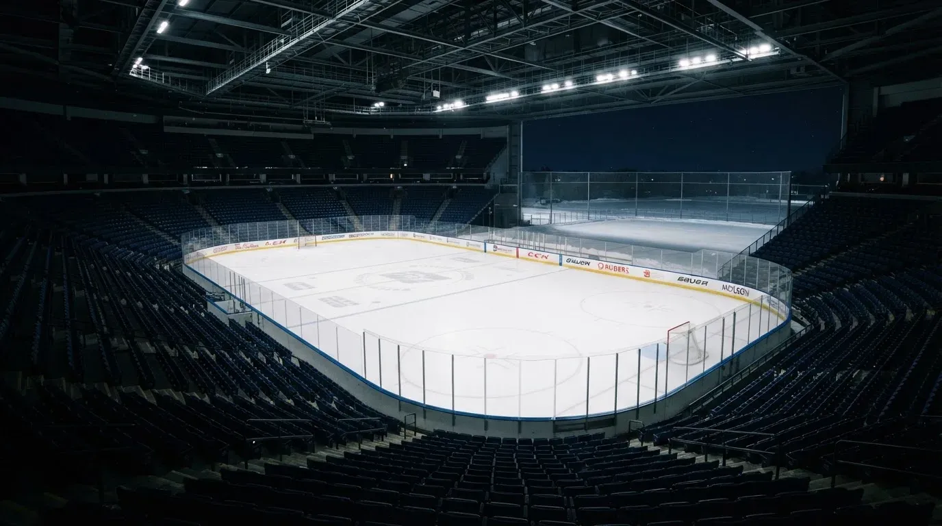 Eine Eishalle von Weitem unter Flutlicht, die leere Eisfläche glänzt, auf den Rängen sitzt niemand, draussen liegt Schnee.