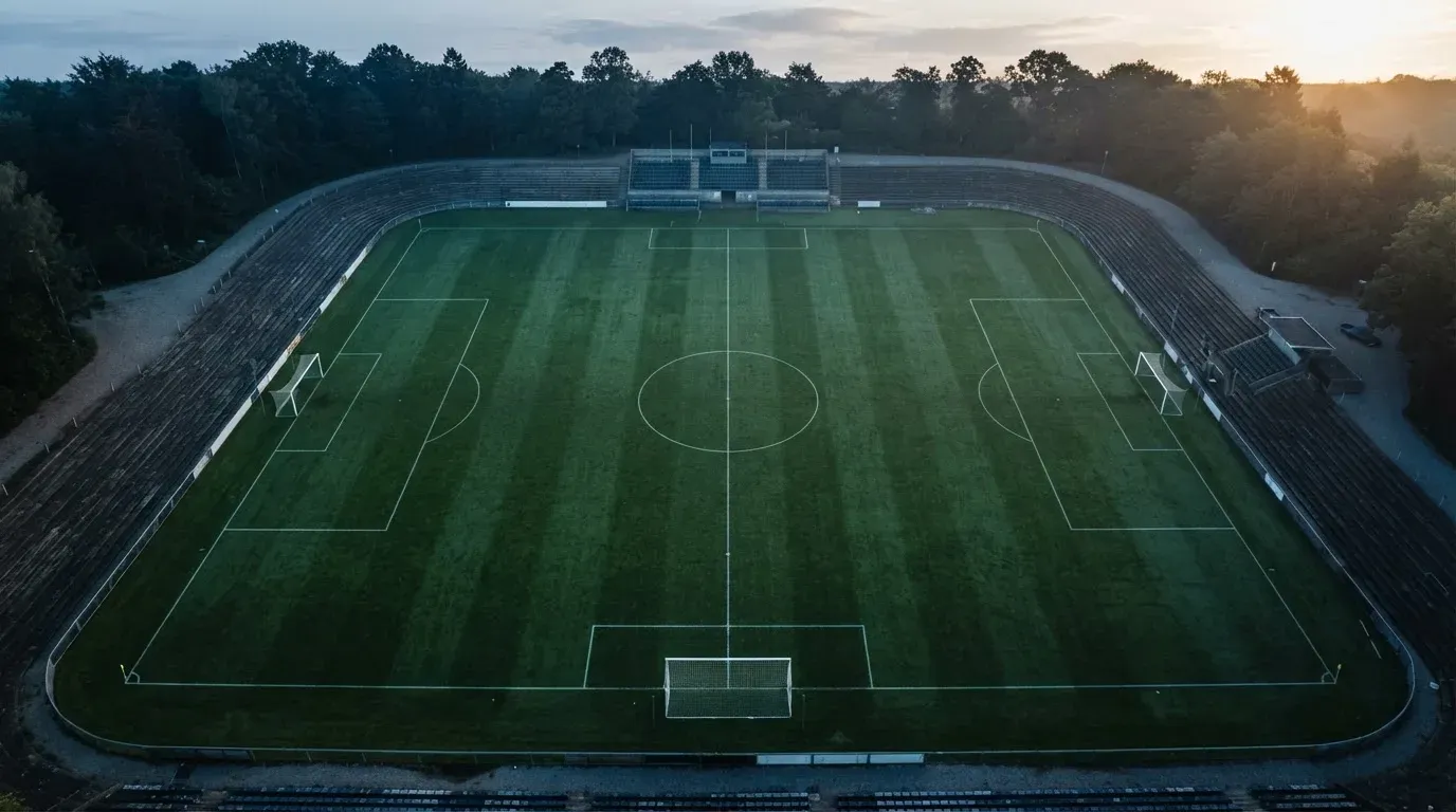 Ein Fussballplatz von oben gesehen, die Linien bilden ein helles Muster auf dem Rasen, Drohnenperspektive in der Morgendämmerung.