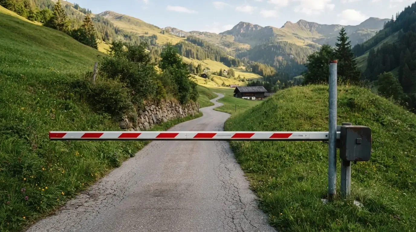 Ein Schlagbaum sperrt eine Landstrasse in den Bergen, dahinter windet sich der Weg zwischen grünen Hängen.