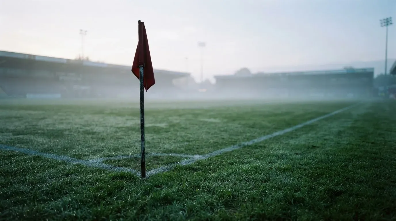 Eine Eckfahne steht am Morgen auf nassem Rasen, Tautropfen hängen im Gras und über dem Platz liegt leichter Dunst.