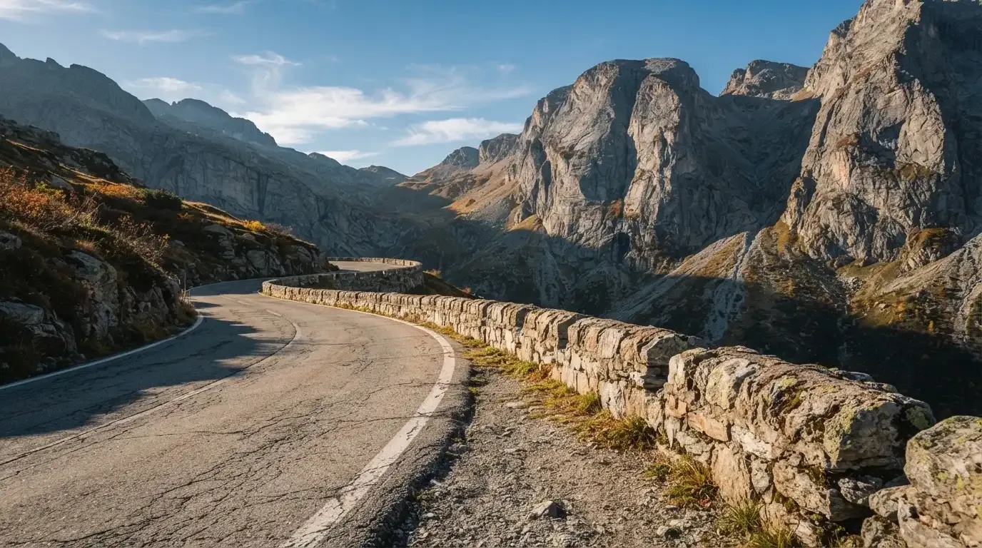 Eine Passstrasse im Hochgebirge säumt eine niedrige Steinmauer, dahinter ragen Felswände auf und der Herbsthimmel ist klar.
