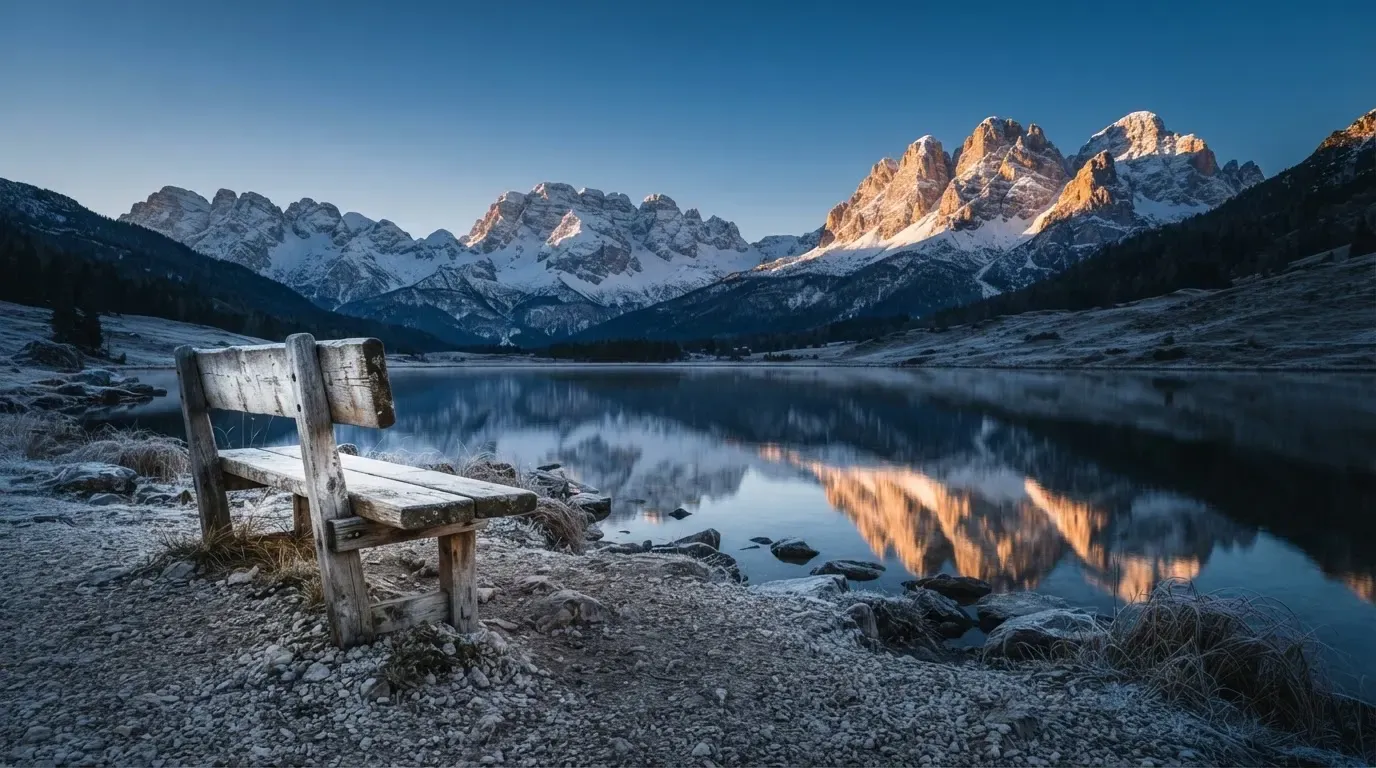 Eine Bank an einem Bergsee, dahinter schneebedeckte Gipfel im klaren Licht eines Wintermorgens.