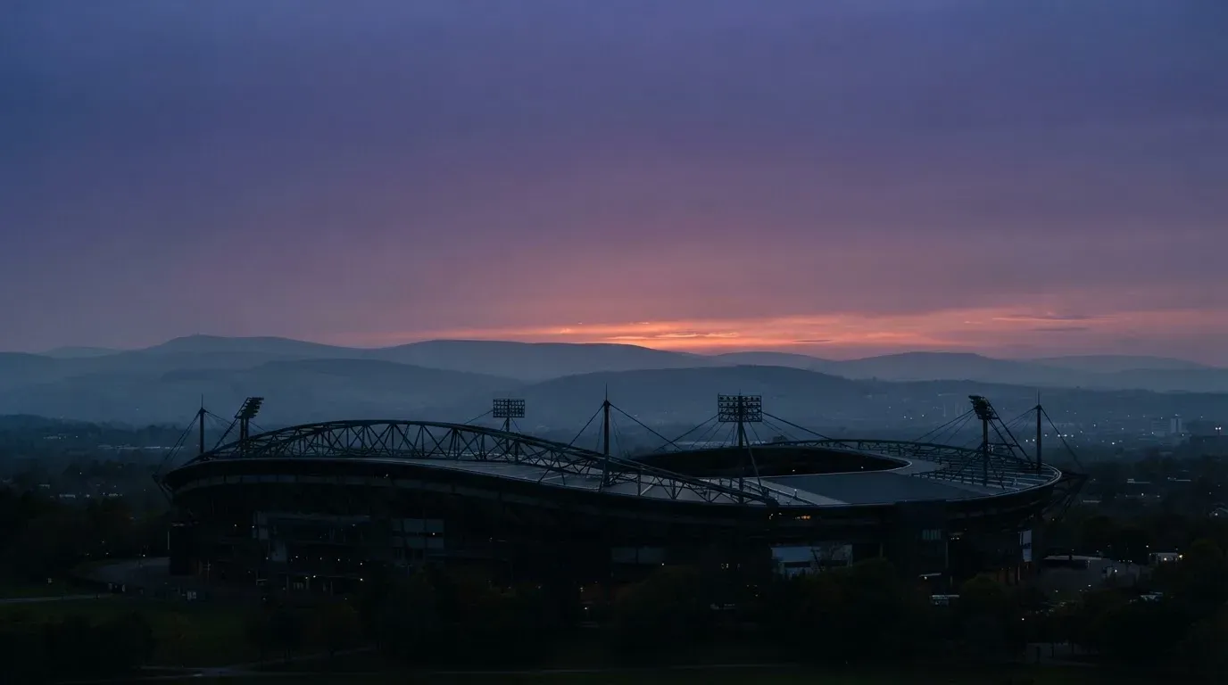 Die Silhouette eines Stadiondachs vor dem violetten Abendhimmel, dahinter eine Hügelkette.