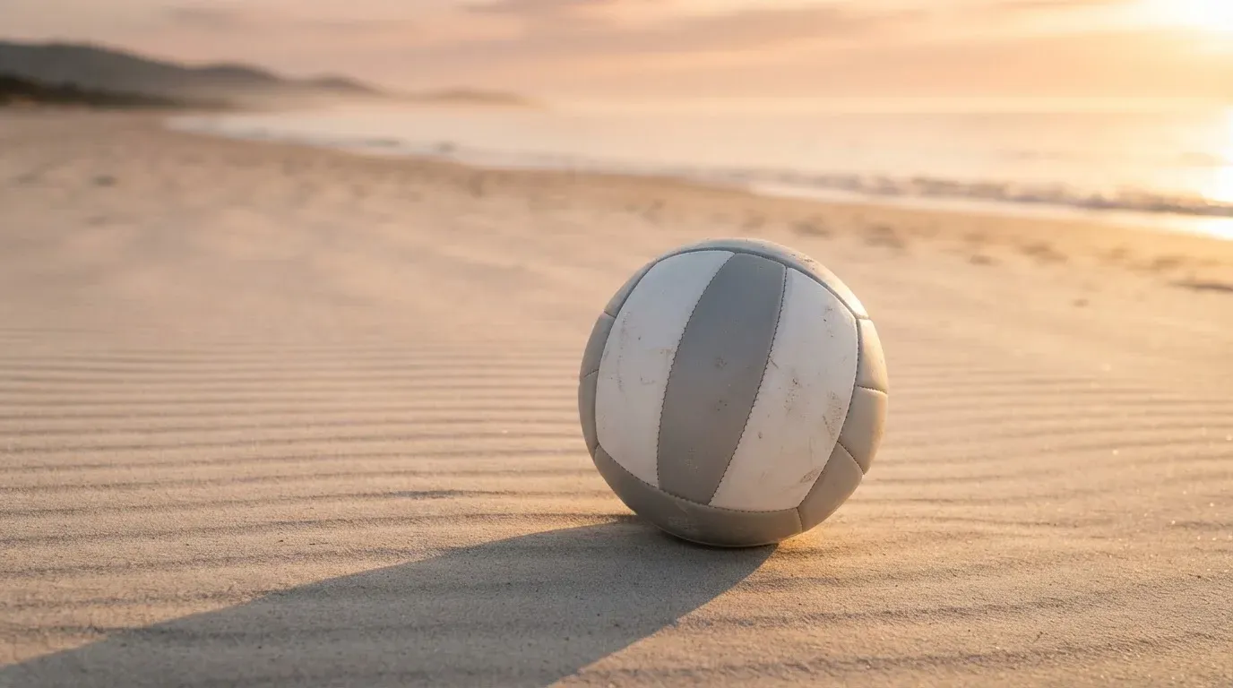 Ein Volleyball liegt auf feinem Sand an einem leeren Strand bei Sonnenaufgang.