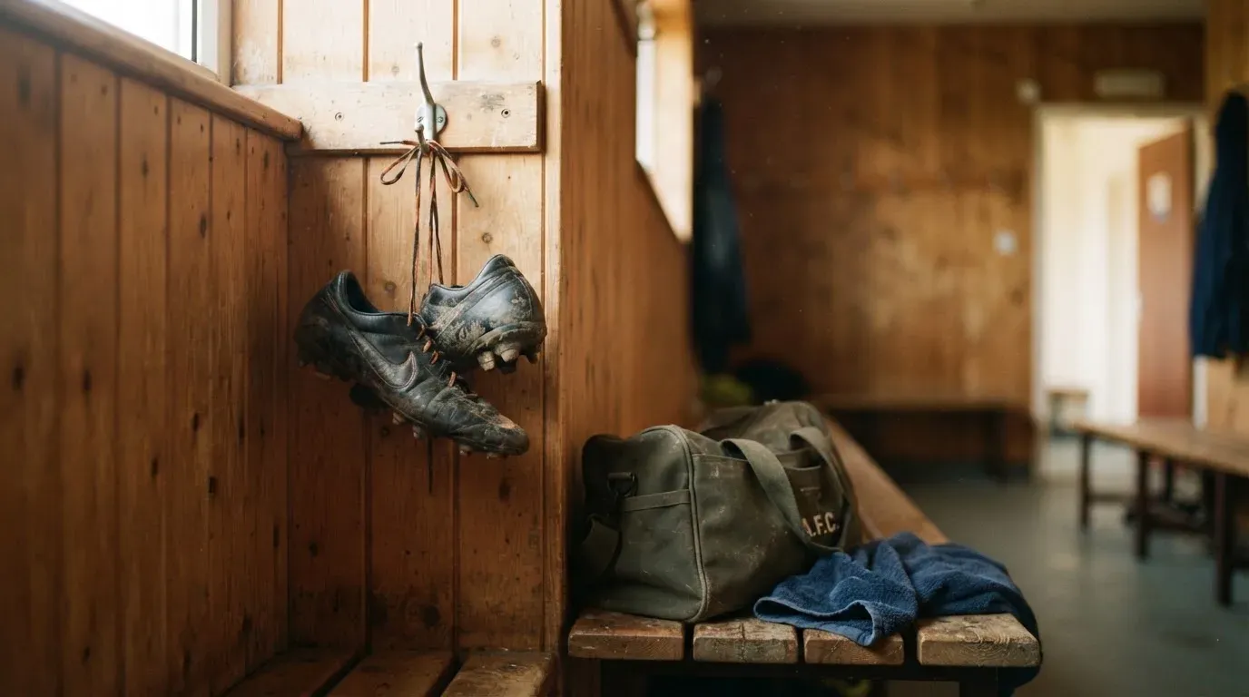 Ein Paar Fussballschuhe hängt an einem Haken in einer ruhigen Umkleide, darunter steht eine Sporttasche auf einer Holzbank.