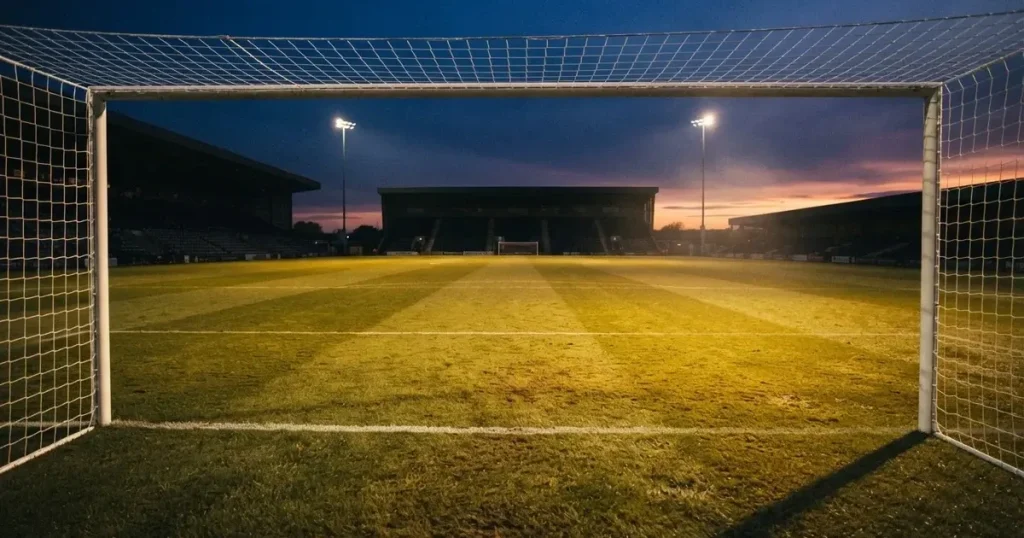 Ein Fussballplatz im Abendlicht mit langen Schatten der Torpfosten, die Rasenfläche leuchtet gelblich.