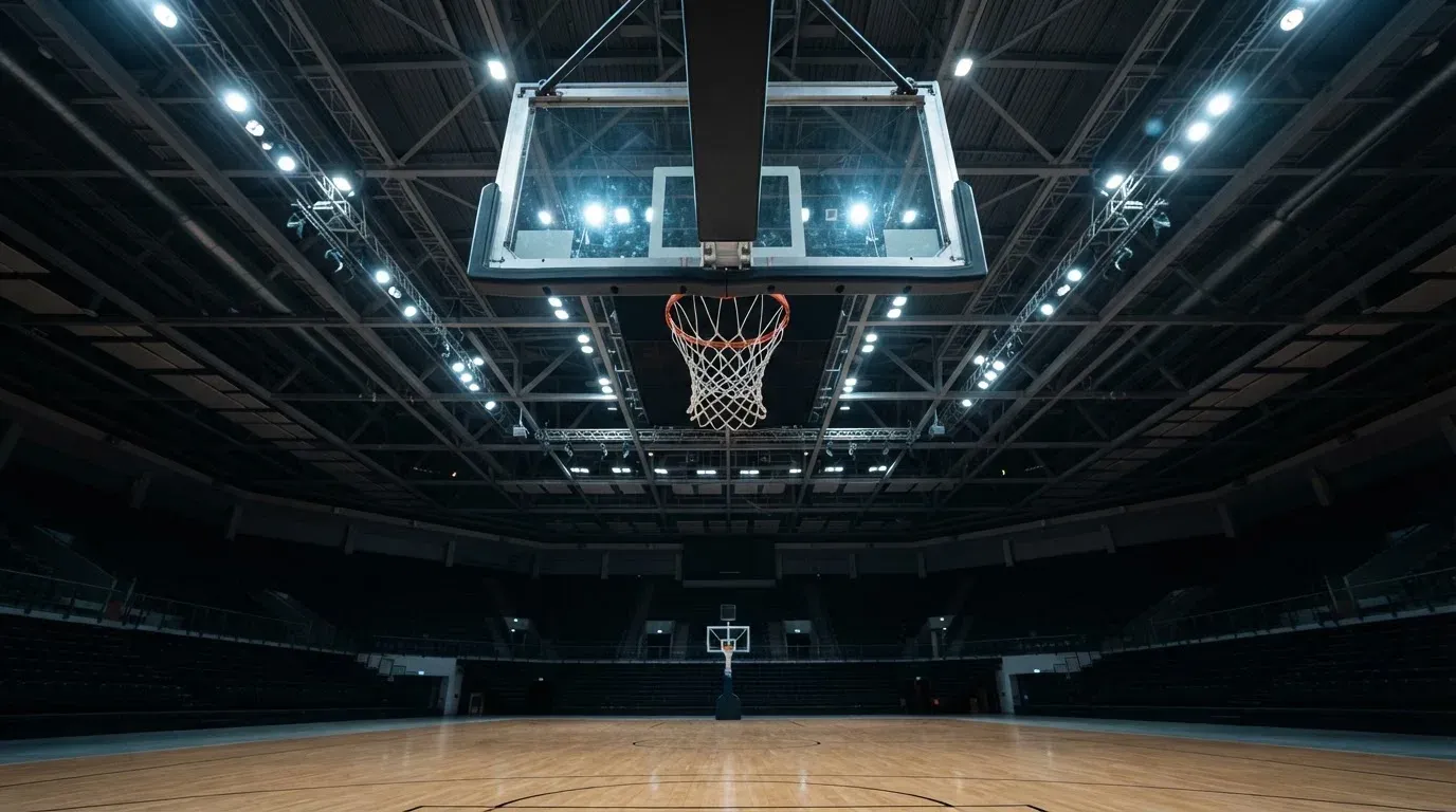 Ein Basketballkorb von unten gesehen, darüber eine Hallendecke mit Scheinwerfern und Stahlträgern.