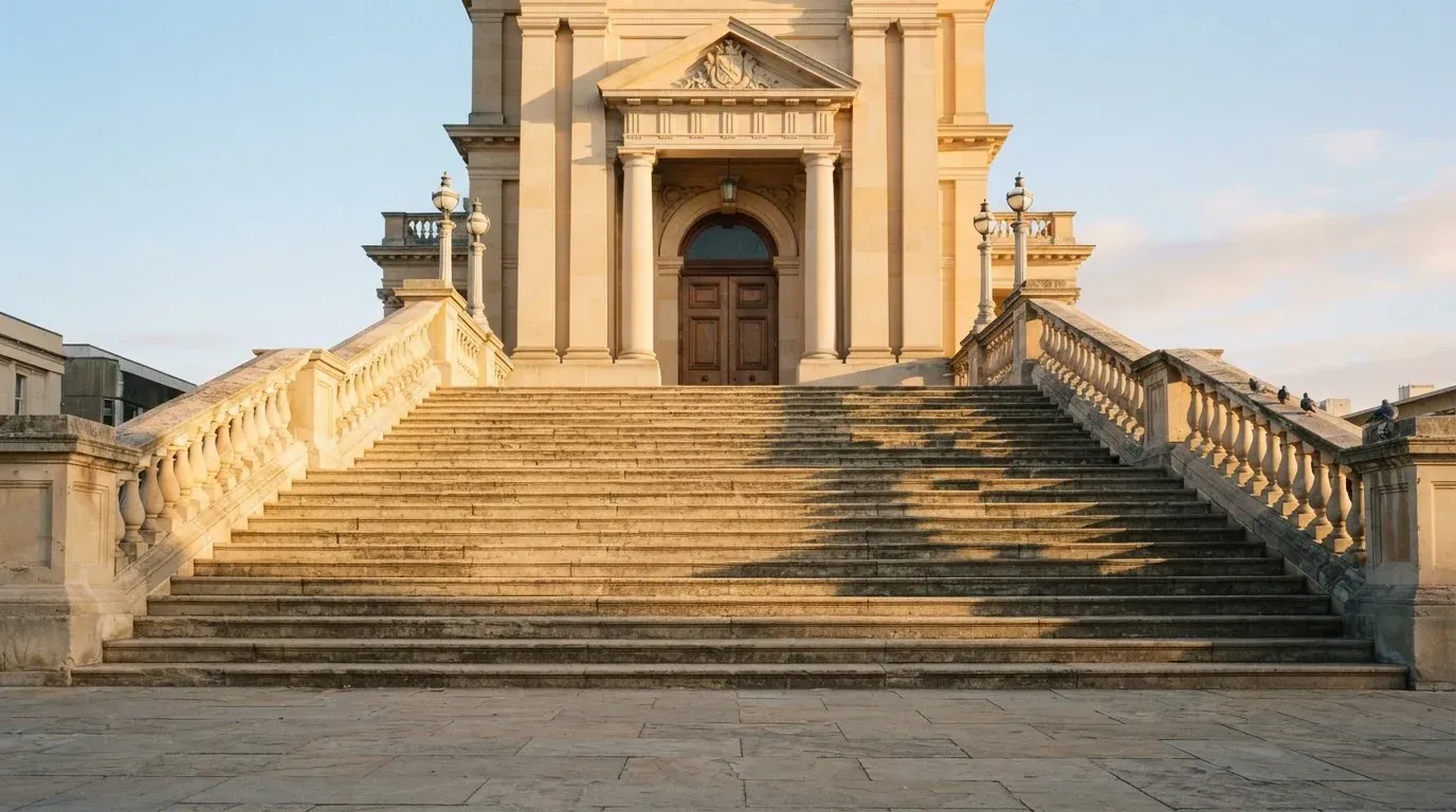 Eine breite Treppe aus Sandstein führt im Morgenlicht zu einem hohen Gebäude.