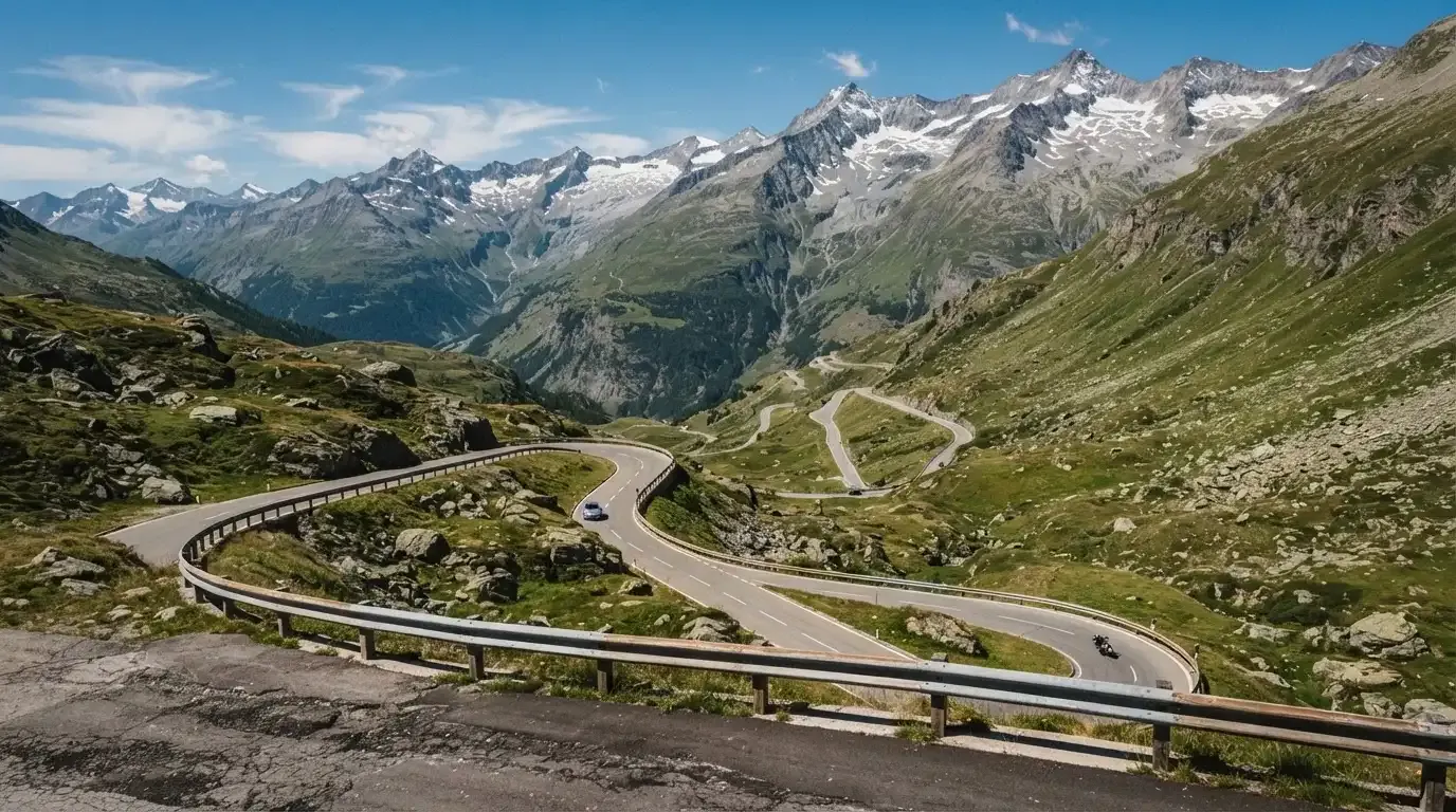 Eine Passstrasse mit Leitplanke windet sich an einem klaren Tag durch eine Berglandschaft.