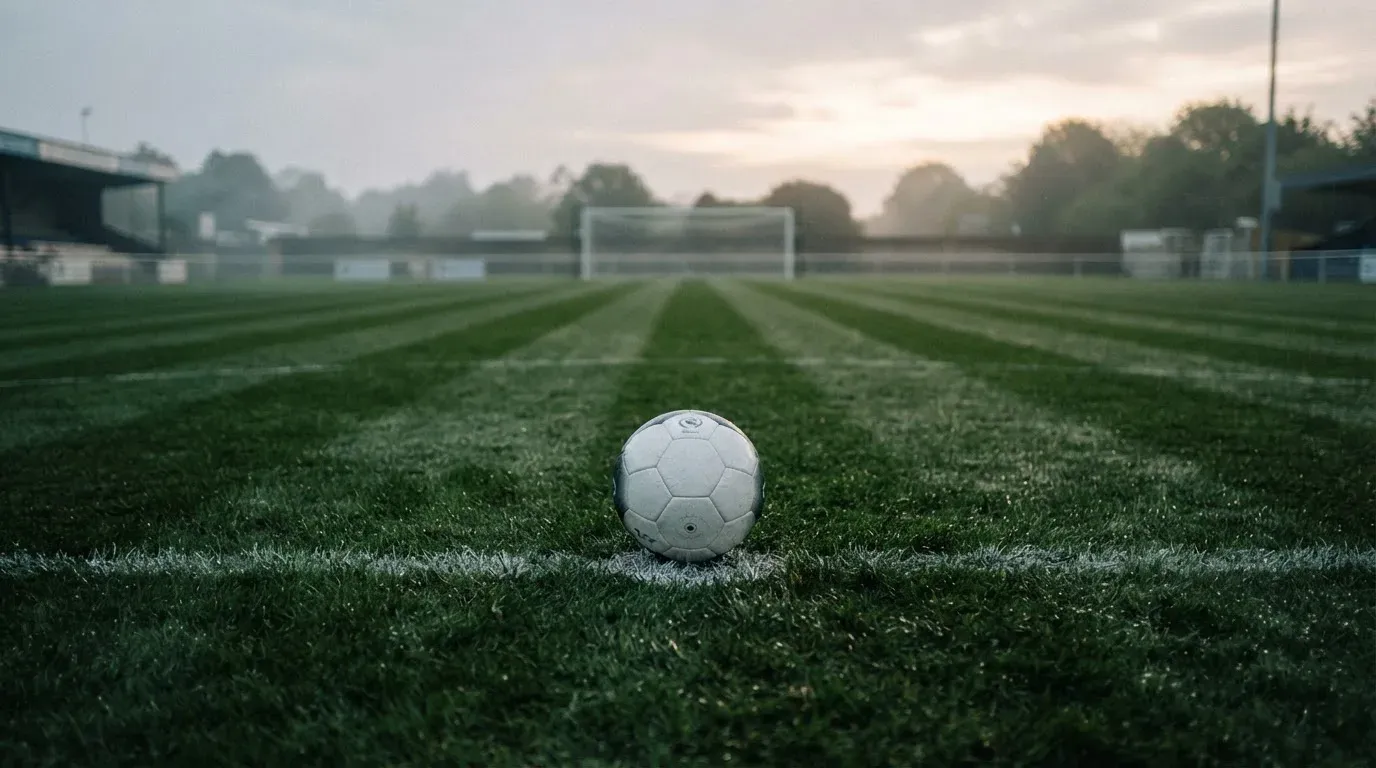 Ein einzelner Fussball liegt auf dem Elfmeterpunkt eines leeren Strafraums, der Rasen glänzt nass.