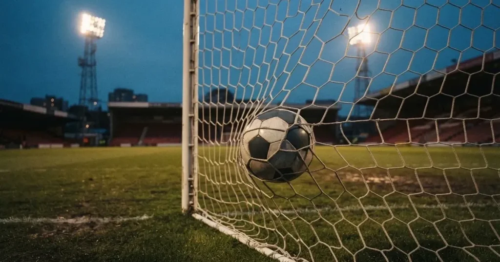 Ein Fussball liegt im Netz eines Tores, Flutlicht und kalte Abendluft liegen über dem leeren Platz