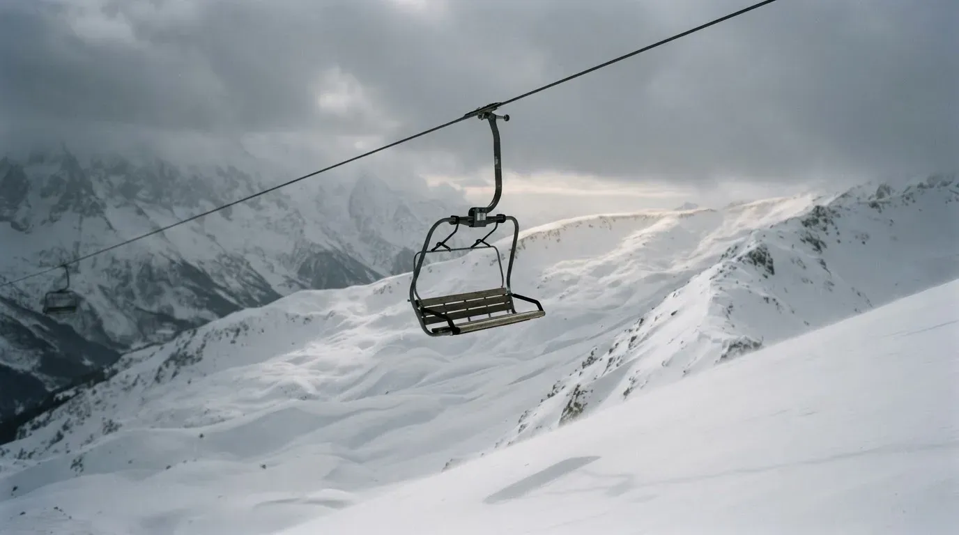 Ein Sessel eines Skilifts schwebt über einer verschneiten Hangkante, dahinter ziehen graue Wolken auf
