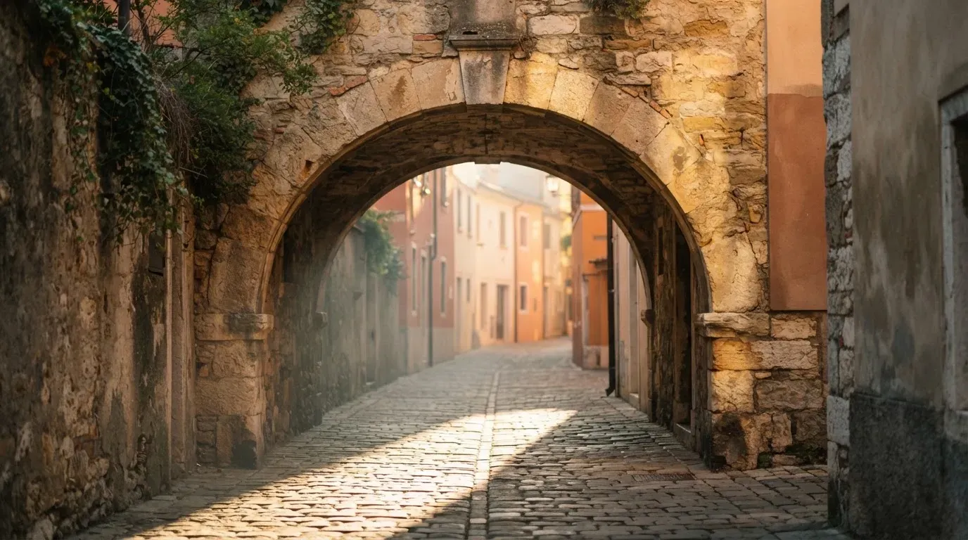 Ein steinerner Torbogen in einer Altstadtgasse, Morgensonne fällt schräg auf das Pflaster