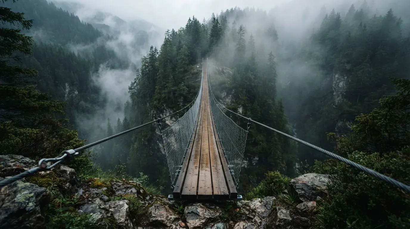 Eine Hängebrücke über eine Schlucht, Nebel steigt auf, dichter Wald bedeckt die steilen Hänge