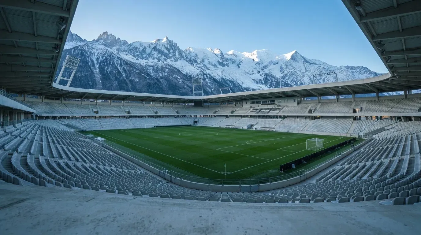 Schneebedeckte Berggipfel erheben sich im klaren Morgenlicht hinter einem leeren Stadion mit hellen Zuschauerrängen.