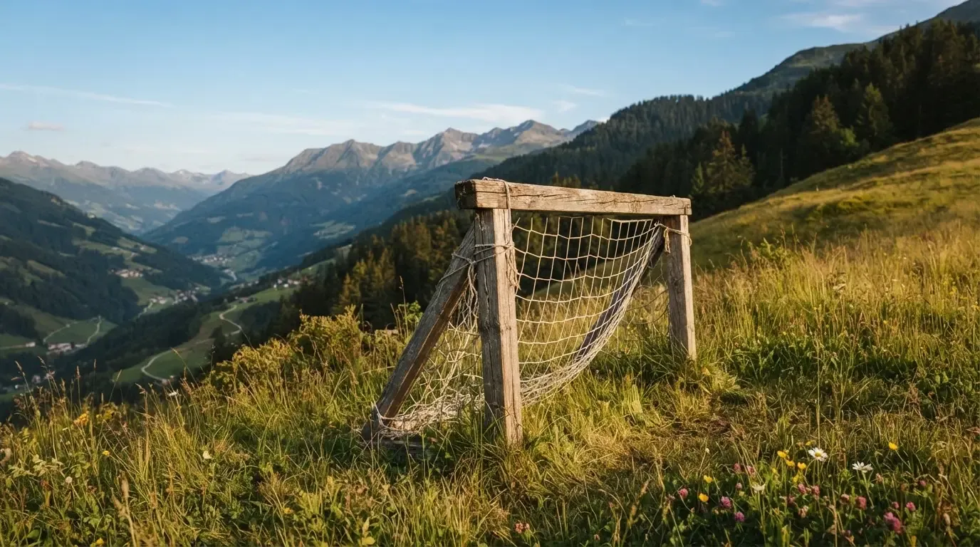 Eine Almwiese mit einem kleinen Holztor für Kinderfussball, dahinter erheben sich bewaldete Hänge im Nachmittagslicht.